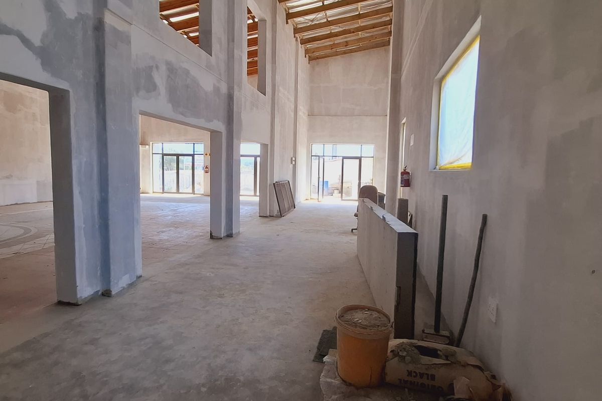 Spacious open-plan interior under construction, featuring double-height ceilings with exposed timber trusses and concrete flooring, offering a blank canvas for custom finishes.