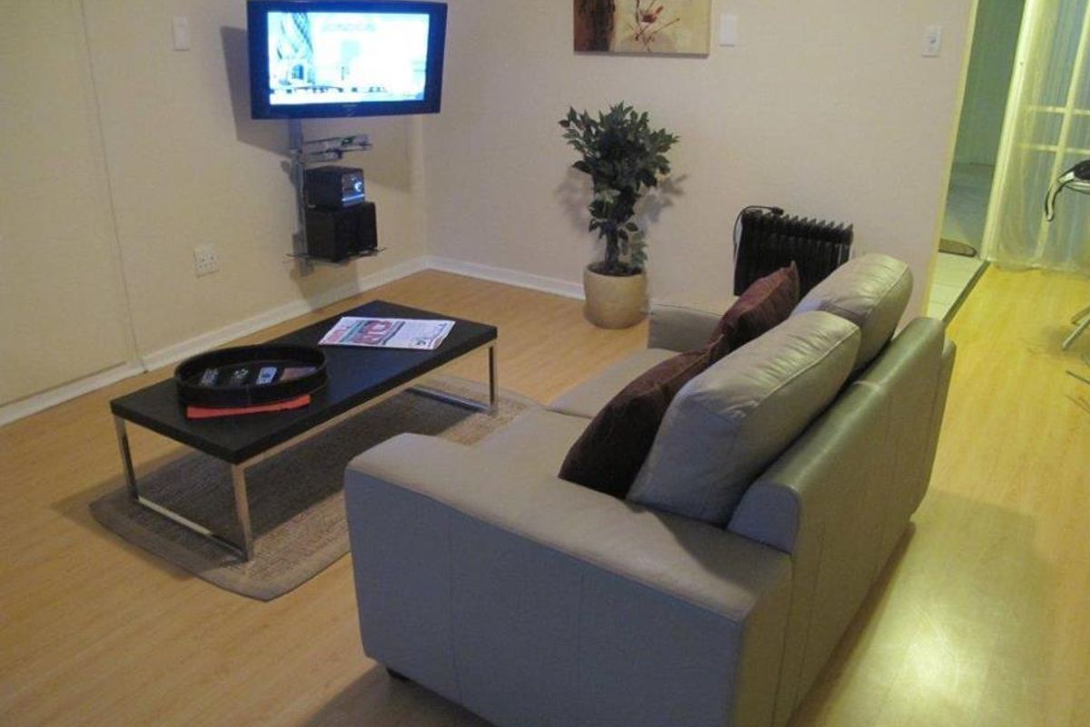A compact living room area featuring light-toned laminate flooring and a wall-mounted television setup.