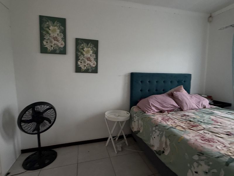 A functional bedroom featuring tiled flooring, a built-in cupboard, and a window with security bars, offering a neutral space ready for personalization.