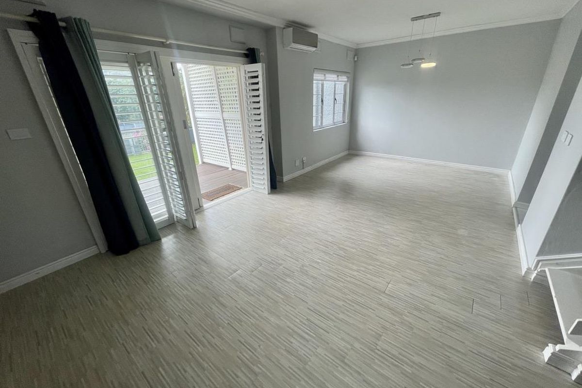 Spacious, light-filled living area featuring modern laminate flooring, split-system air conditioning, and plantation shutters with direct access to an outdoor patio.