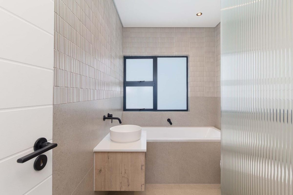 Modern bathroom featuring a floating vanity with a vessel sink, built-in bathtub, matte black fixtures, and textured wall tiling.