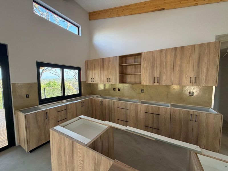 Modern kitchen under construction featuring wood-grain cabinetry, exposed timber beams, and a metallic splashback, awaiting final countertop installation and appliance fitting.