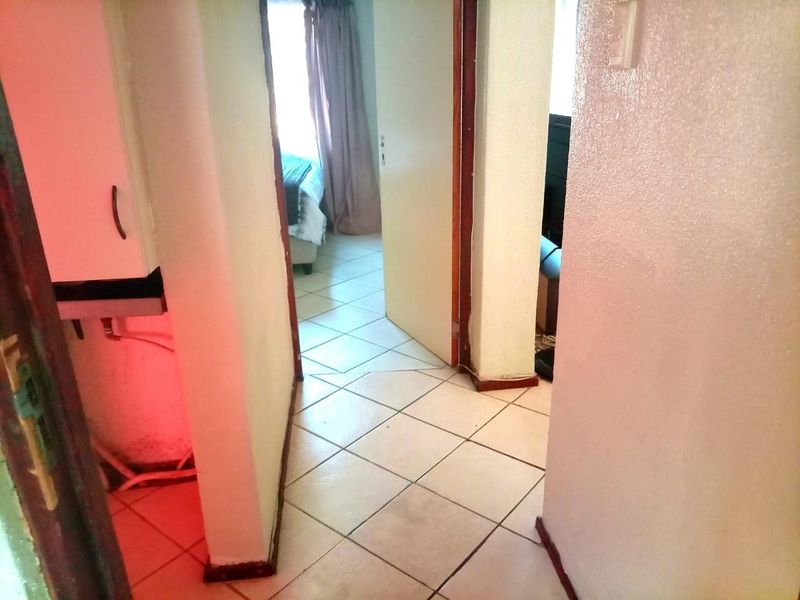 A narrow interior hallway with ceramic floor tiles connecting to adjacent rooms, showing signs of wear on the door frames and walls.