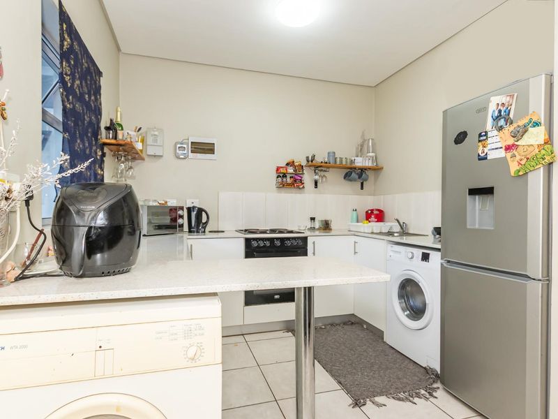 Compact kitchen featuring white cabinetry, laminate countertops, tiled splashback, and integrated space for laundry appliances.