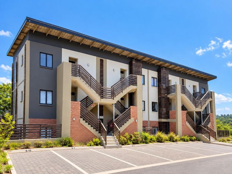 Modern apartment building exterior featuring brick and plaster facade, timber detailing, external staircases, and designated paved parking bays.