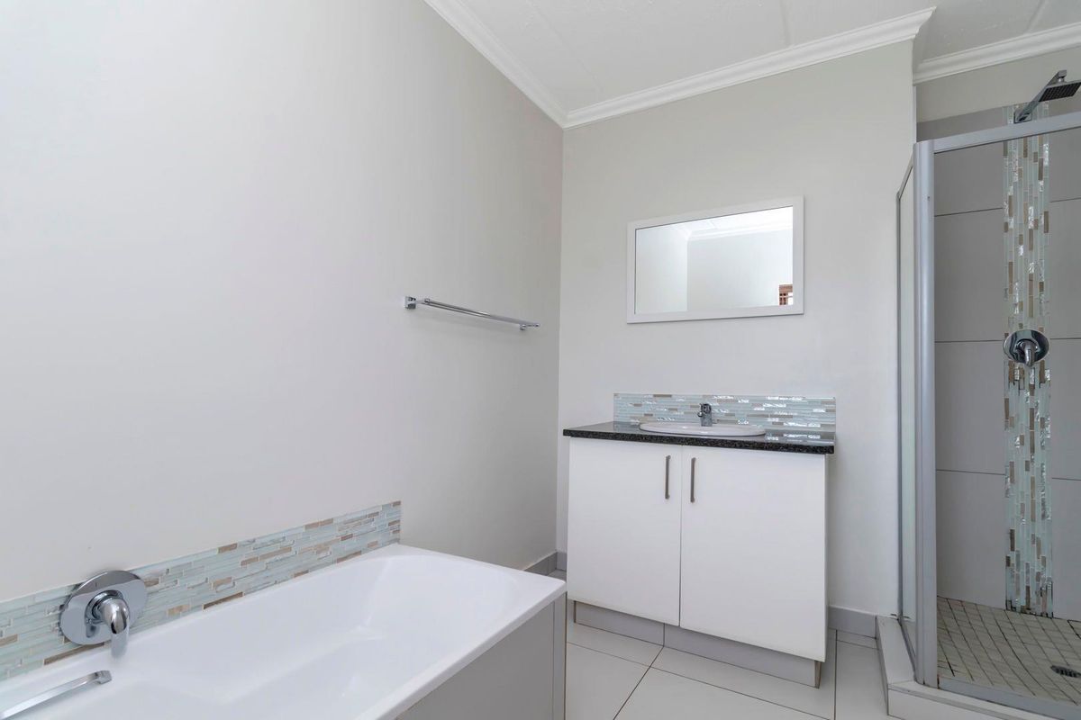 A clean, modern bathroom featuring a white vanity with a dark countertop, a separate bathtub, and a glass-enclosed shower with mosaic tile accents.