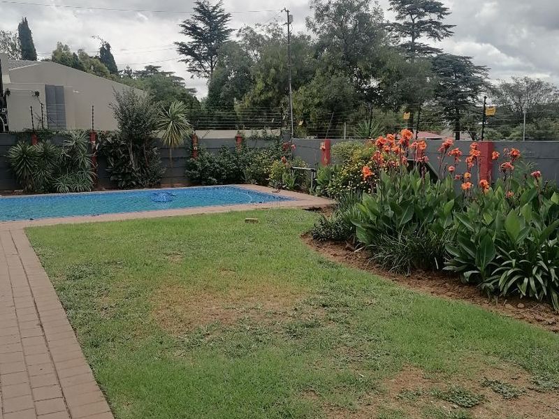A private outdoor pool area featuring a paved walkway, established garden beds, and secure perimeter walling with electric fencing.
