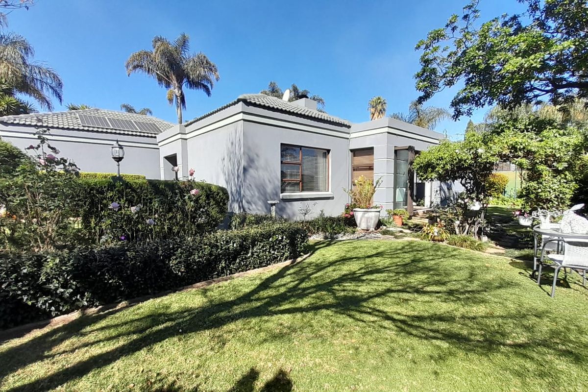 A well-maintained rear exterior view of the cluster home featuring a landscaped garden, manicured hedging, and a tiled roof with solar panels.