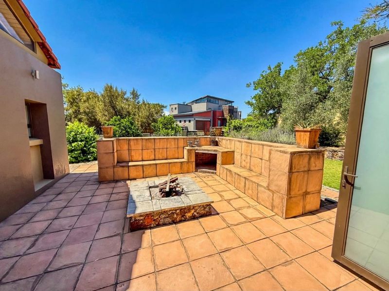 Outdoor patio area featuring a built-in tiled seating bench, a stone-clad fire pit, and a built-in braai, perfect for alfresco entertaining.