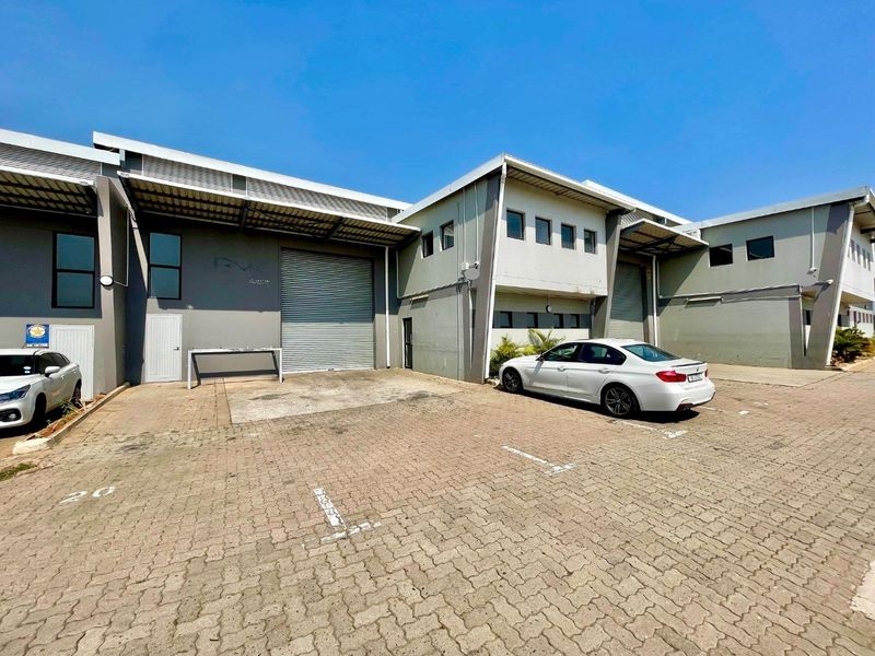 Front exterior view of an industrial warehouse unit featuring roller shutter doors, paved parking area, and a functional metal roof structure.