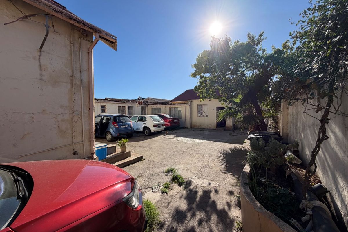 Rear courtyard area featuring a concrete driveway and perimeter walls, showing significant signs of wear and maintenance requirements.