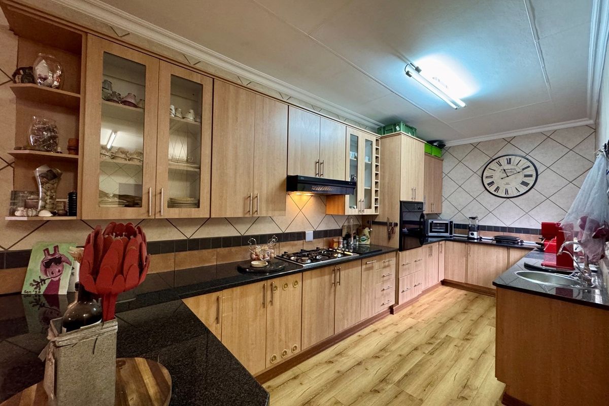 A functional kitchen featuring light wood-look cabinetry, dark granite countertops, a built-in oven, gas hob, and tiled backsplash with laminate flooring.