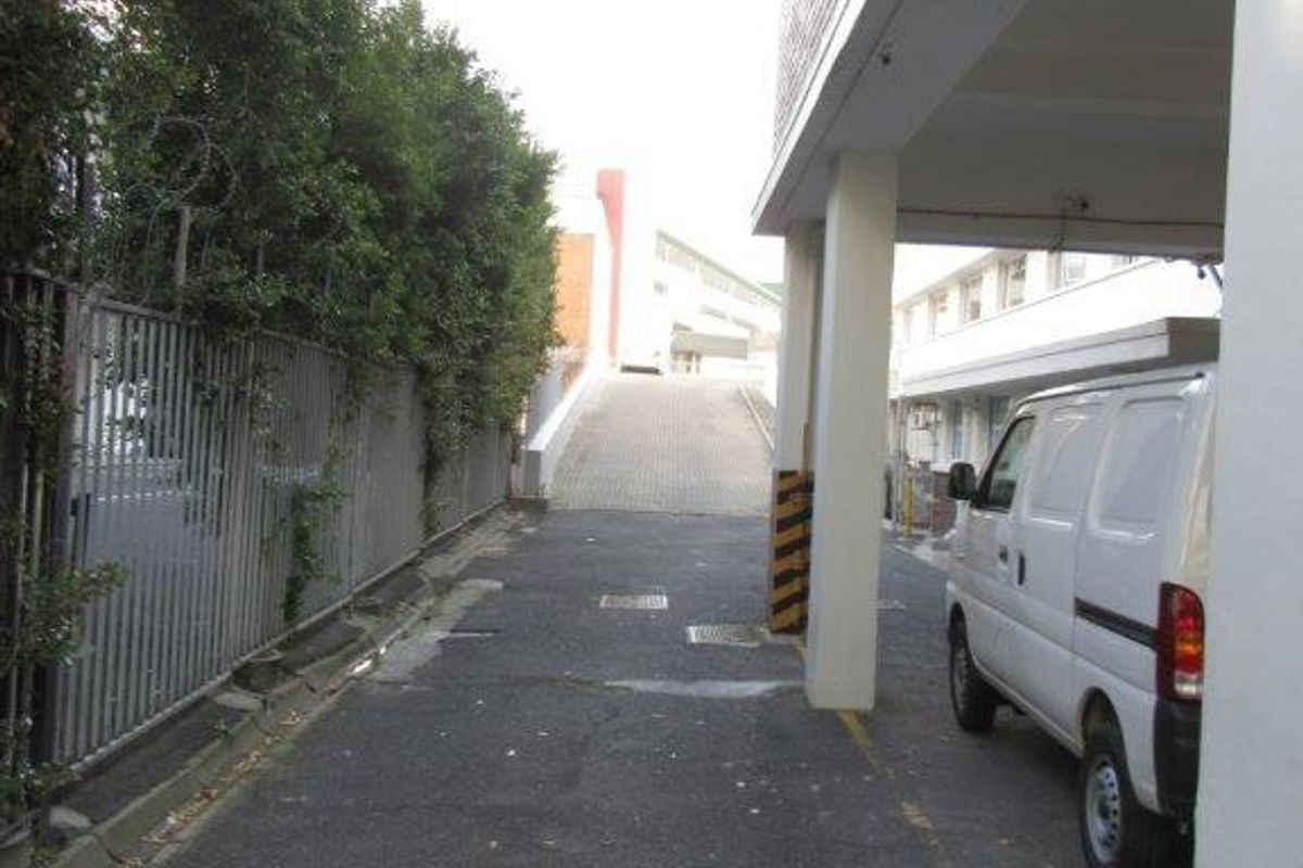 A paved rear access driveway featuring concrete support columns, metal security fencing, and a concrete ramp leading to the upper level of the property.