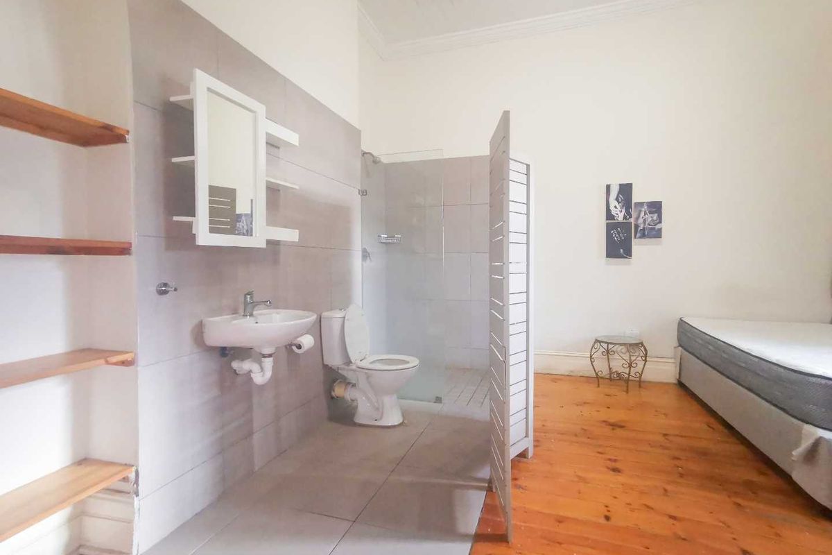 Bedroom featuring an open-plan en-suite bathroom area with a wall-mounted basin, toilet, and glass-enclosed shower, complemented by timber flooring and built-in shelving.