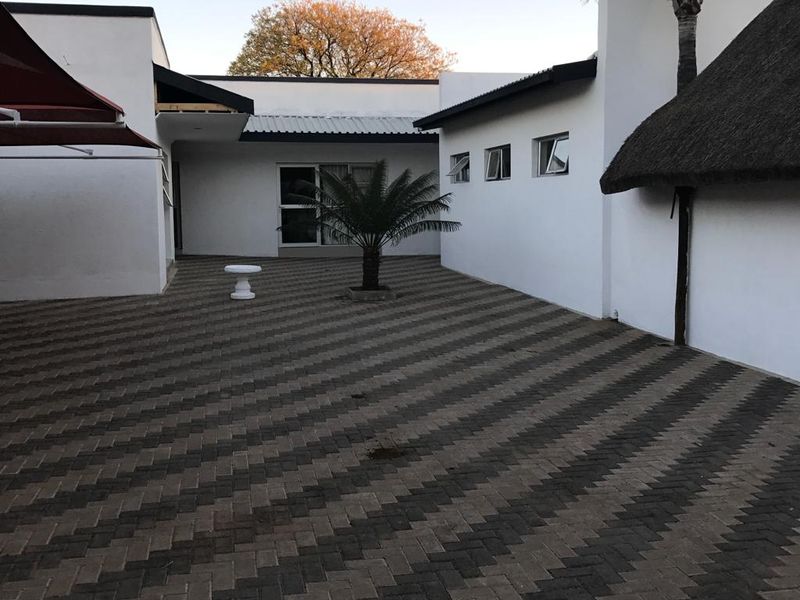A paved rear courtyard area featuring a mix of modern white building facades, a thatched roof section, and an outdoor awning.