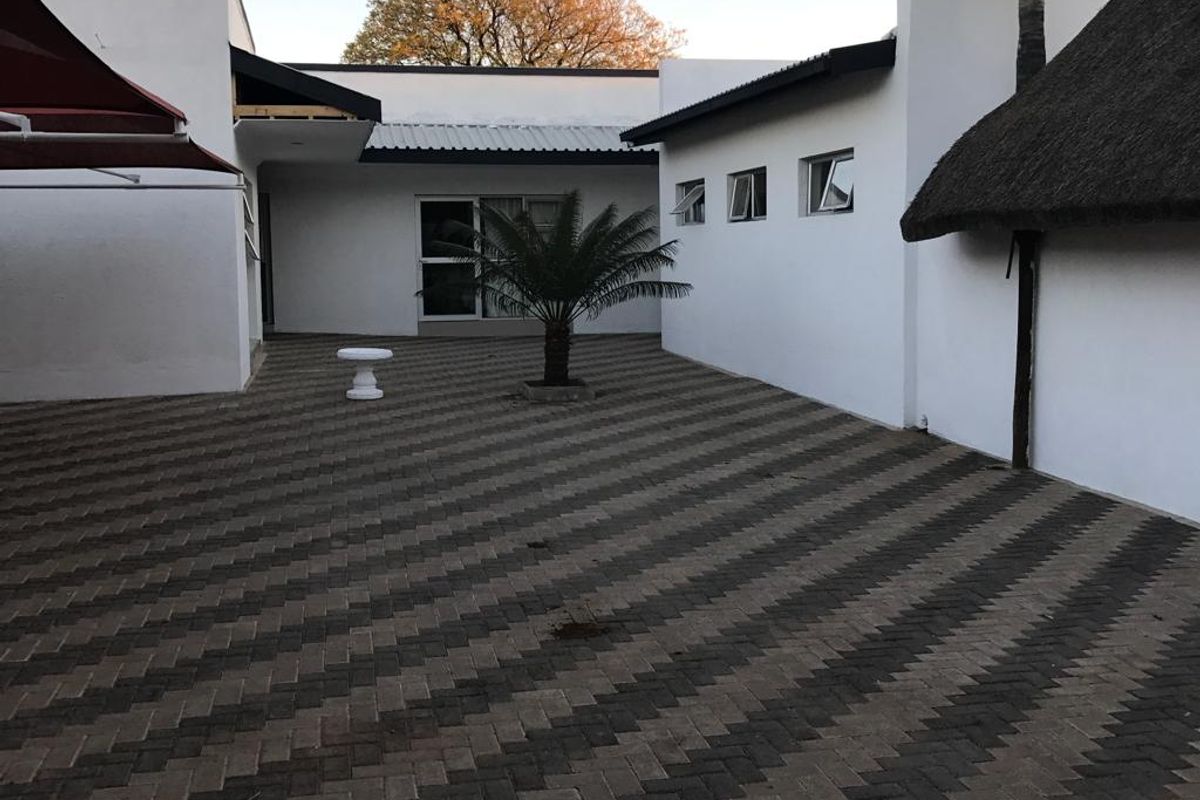 A paved rear courtyard area featuring a mix of modern white building facades, a thatched roof section, and an outdoor awning.