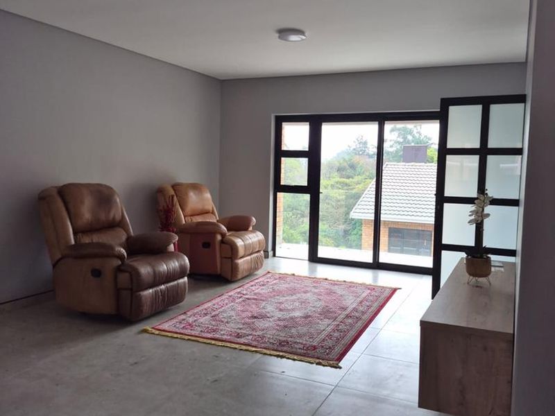 A living room featuring large sliding glass doors, neutral tiled flooring, and a modern black-framed glass partition.