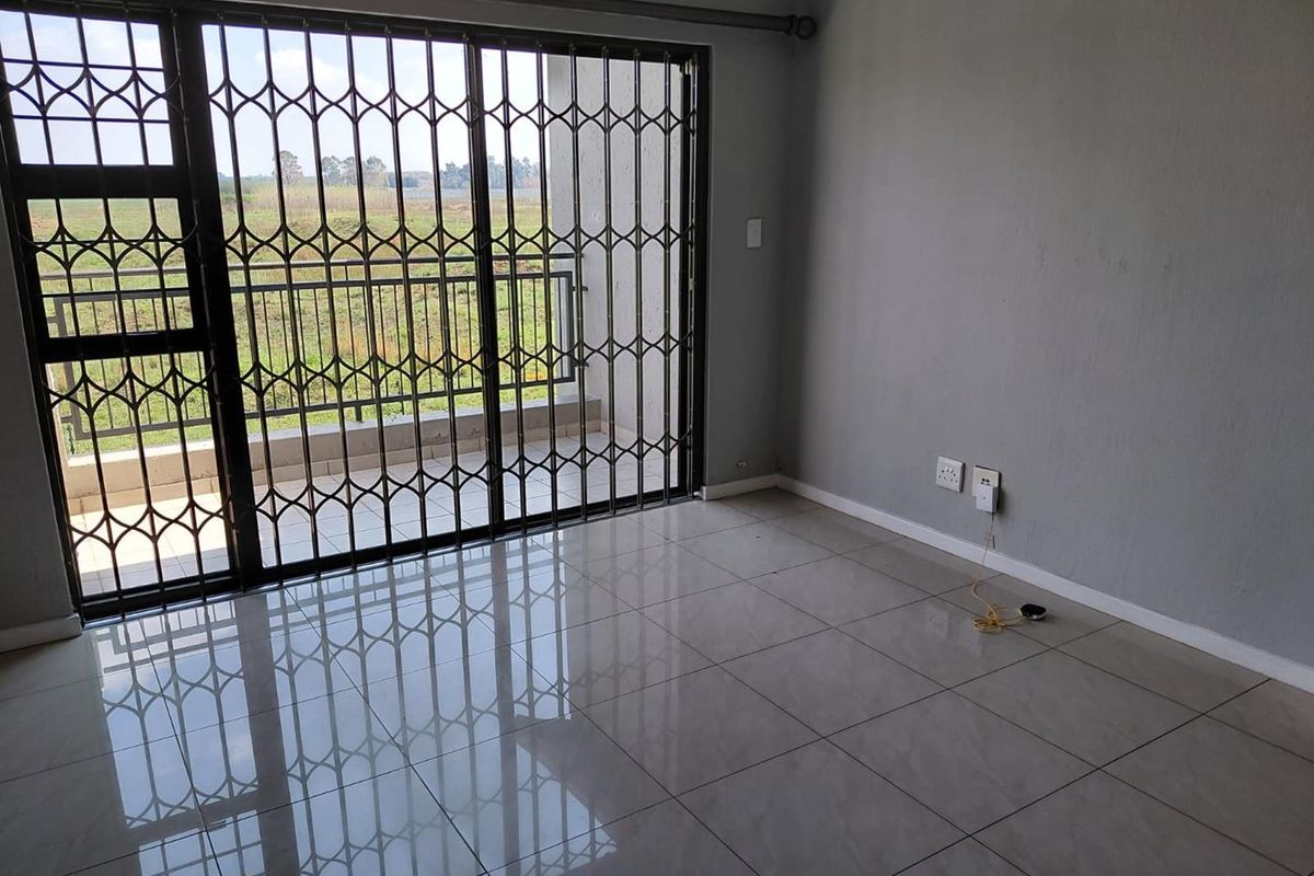 An empty living room featuring tiled flooring, neutral grey walls, and a sliding glass door with a security gate leading to a balcony.