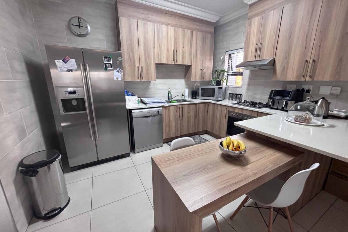 Modern kitchen featuring wood-look cabinetry, stone countertops, integrated breakfast nook, stainless steel appliances, and tiled flooring.