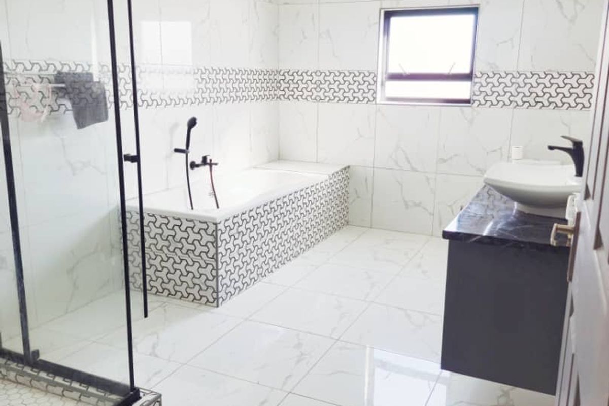 Modern bathroom featuring a glass-enclosed shower, a tiled bathtub with decorative accents, and a floating vanity with a vessel sink.