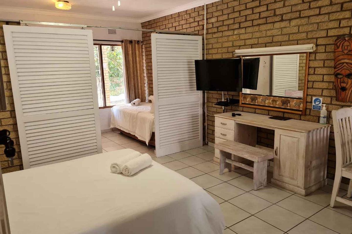 A bedroom featuring exposed brick walls, tiled flooring, and sliding louvered room dividers separating the sleeping areas.