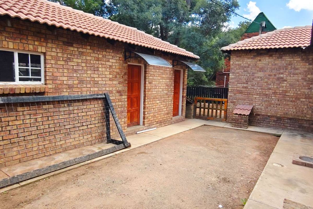 A rear exterior view of the property featuring face-brick walls, terracotta roof tiles, and a paved courtyard area with access doors.
