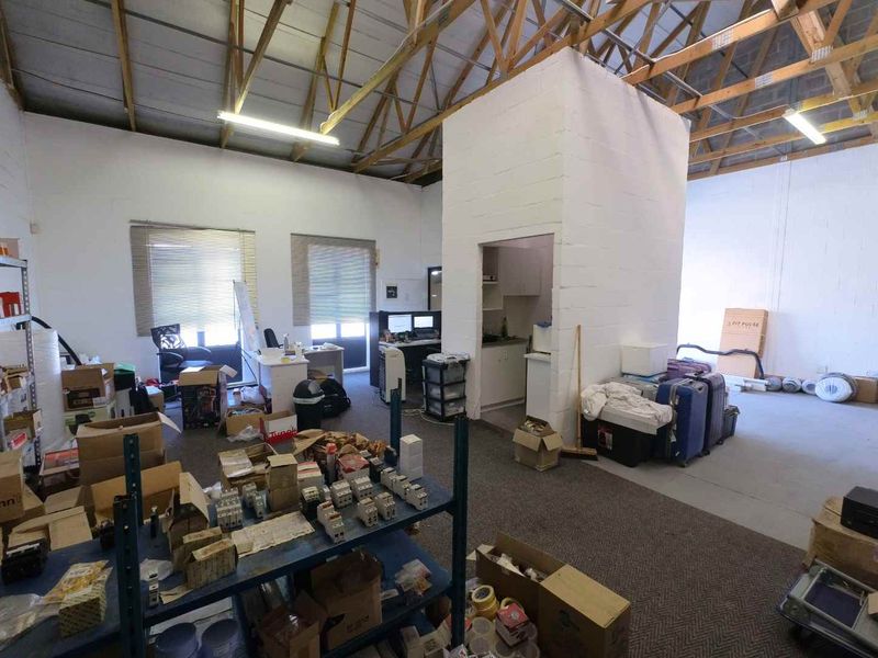 Industrial utility space featuring exposed timber roof trusses, fluorescent lighting, and a central concrete block partition with a small built-in kitchenette area.