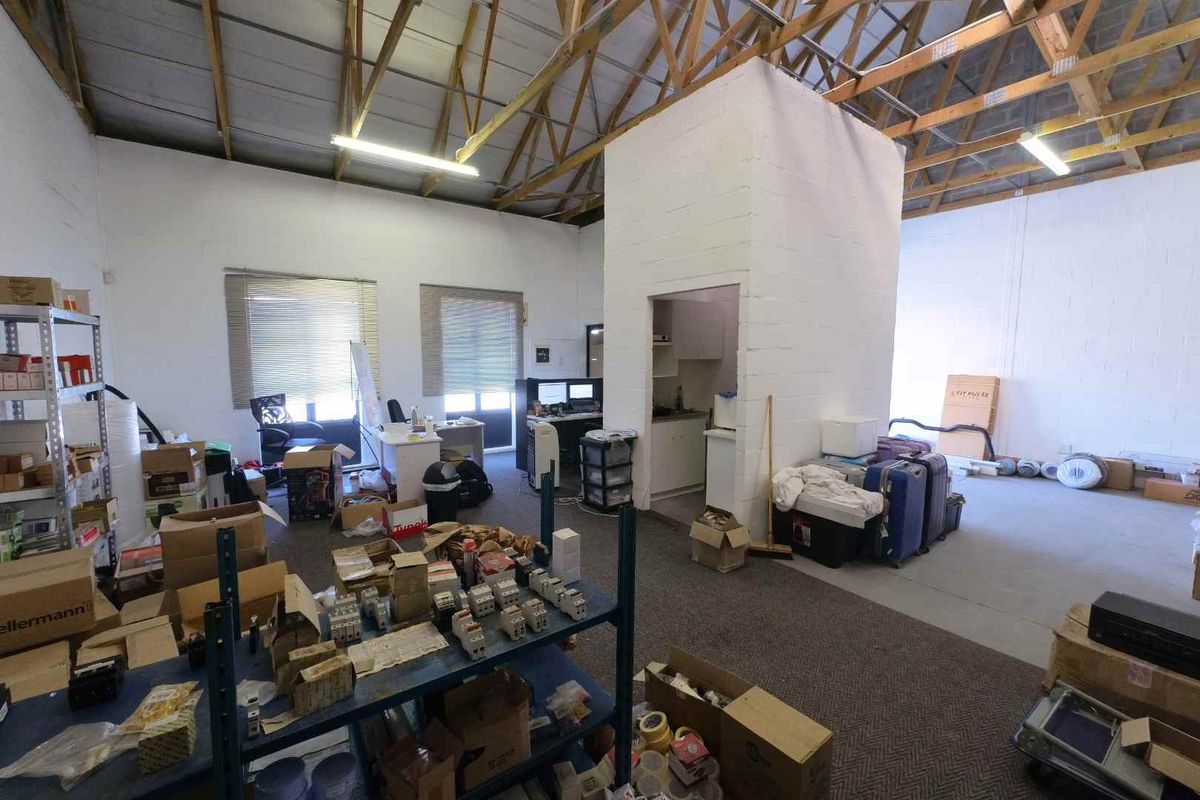 Industrial utility space featuring exposed timber roof trusses, fluorescent lighting, and a central concrete block partition with a small built-in kitchenette area.