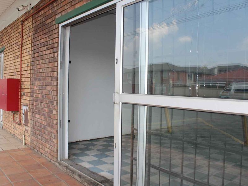 Exterior view of a retail storefront featuring a brick facade, tiled patio area, and a sliding glass entrance door.