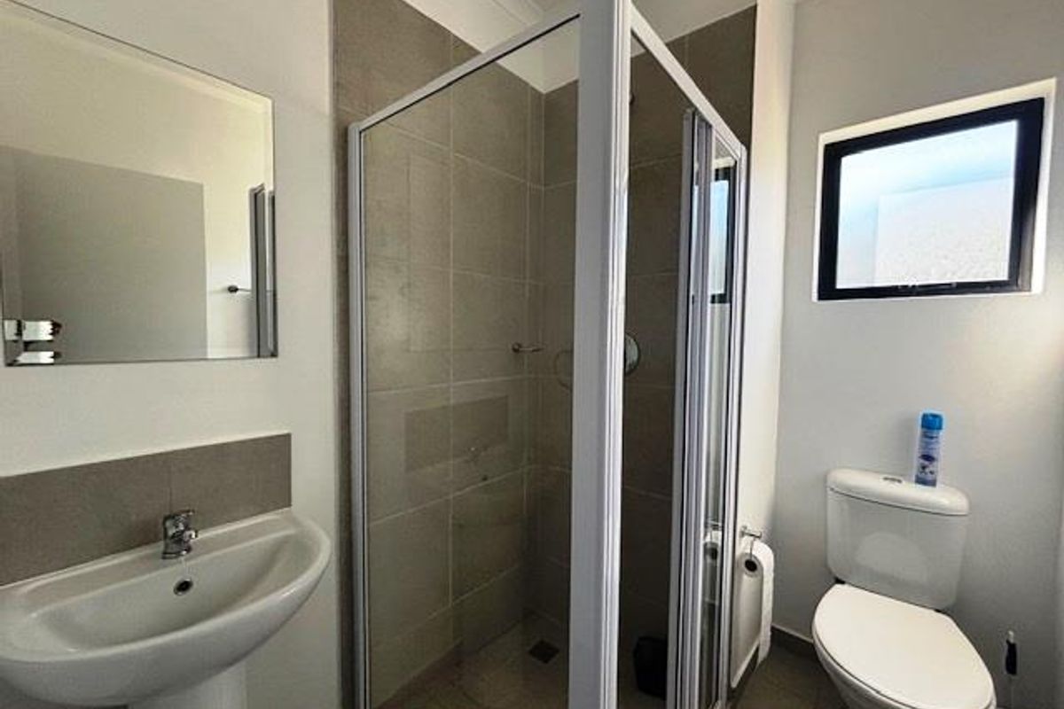 A clean, functional bathroom featuring a pedestal sink, a glass-enclosed shower with tiled walls, and a standard toilet.