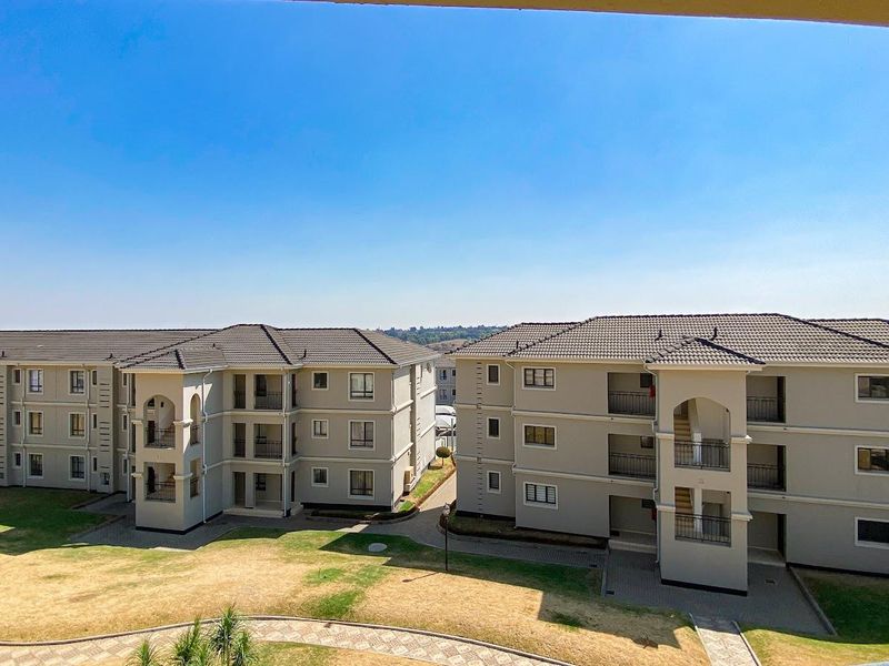 An elevated view of the apartment complex featuring multi-story buildings with tiled roofs, private balconies, and well-maintained communal garden areas.
