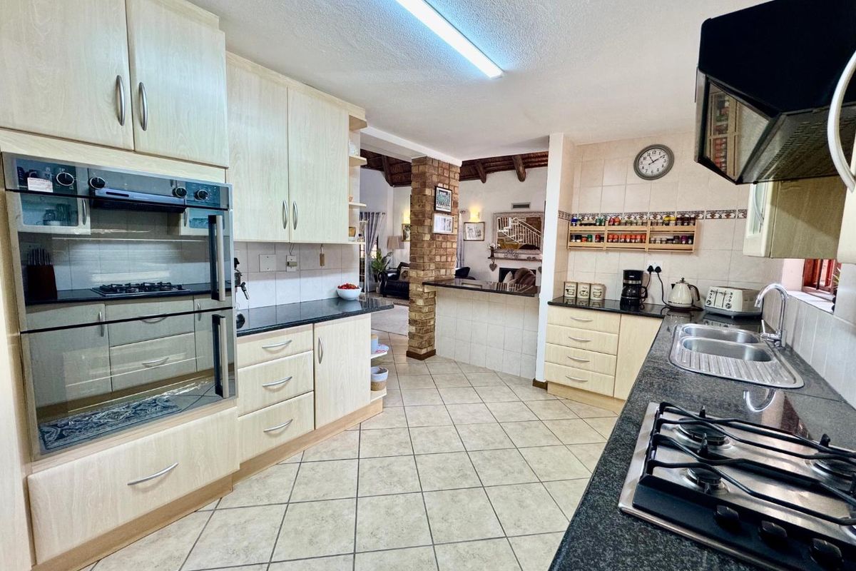 A functional kitchen featuring light wood cabinetry, dark granite countertops, a built-in oven, gas hob, and an open-plan layout connecting to the living area.