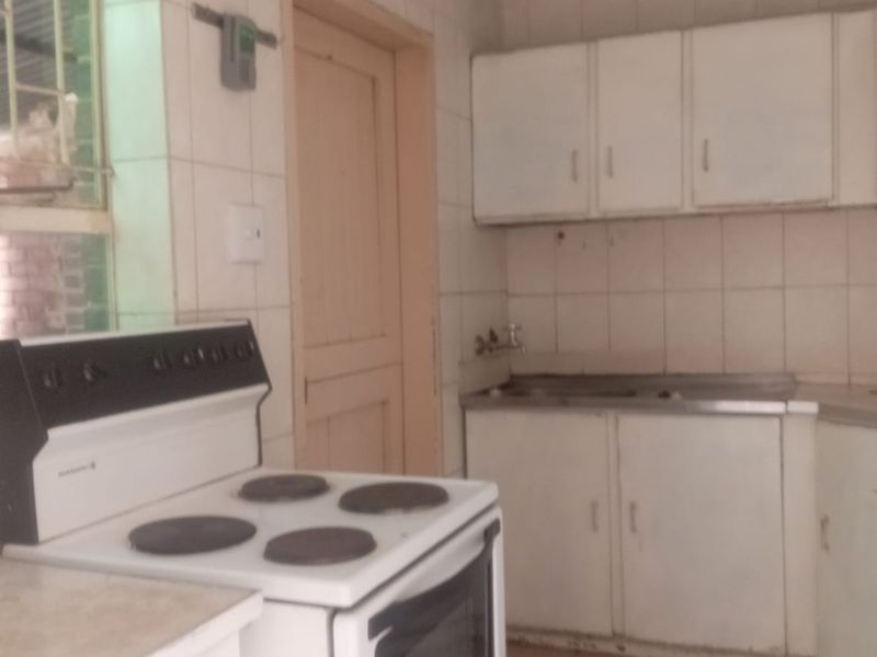 A functional kitchen featuring tiled flooring, wall-mounted cabinetry, and a stainless steel sink, offering a dated aesthetic ready for modernization.