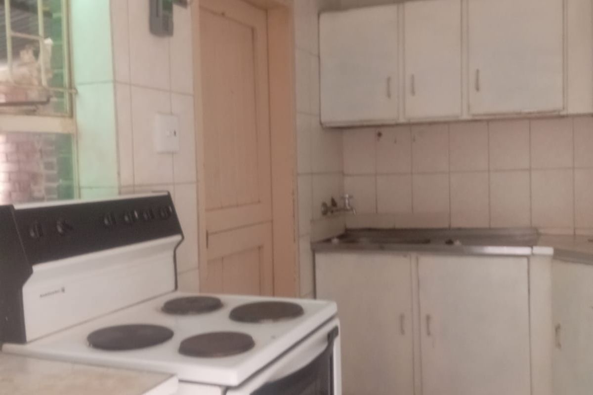 A functional kitchen featuring tiled flooring, wall-mounted cabinetry, and a stainless steel sink, offering a dated aesthetic ready for modernization.