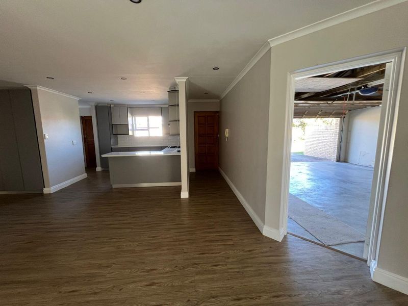 Spacious open-plan living area featuring modern laminate flooring, recessed lighting, and a functional kitchen with built-in cabinetry and an island, leading to a garage.