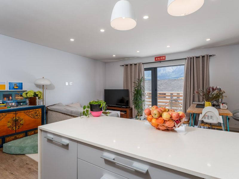 Open plan living area featuring a modern kitchen island with stone countertop, recessed lighting, and access to an outdoor balcony through sliding glass doors.