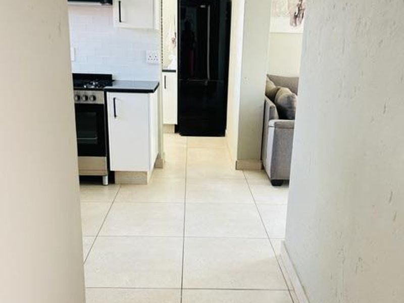 A clean, functional kitchen featuring white cabinetry, a gas stove with extractor fan, and light-toned tiled flooring.