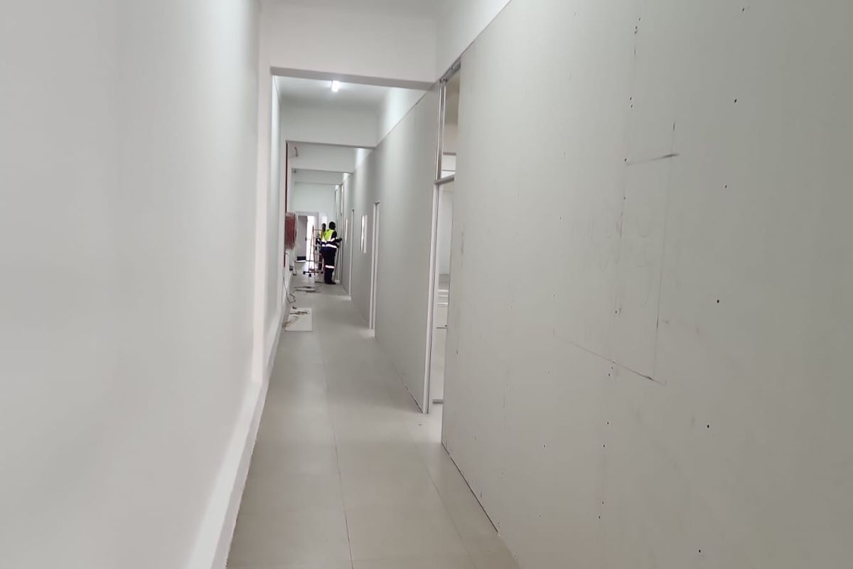 A long office hallway currently under construction, featuring tiled flooring and unfinished drywall partitions awaiting final paint and trim.