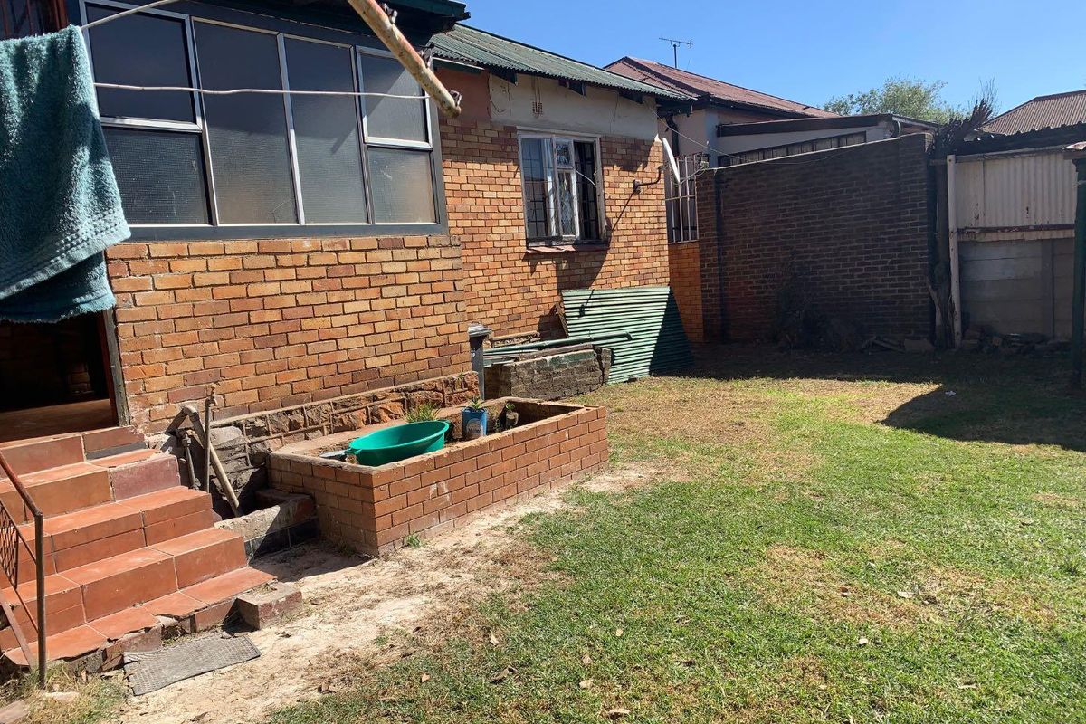Rear exterior view of a brick house featuring a small garden area, raised brick planter, and access steps to the dwelling.