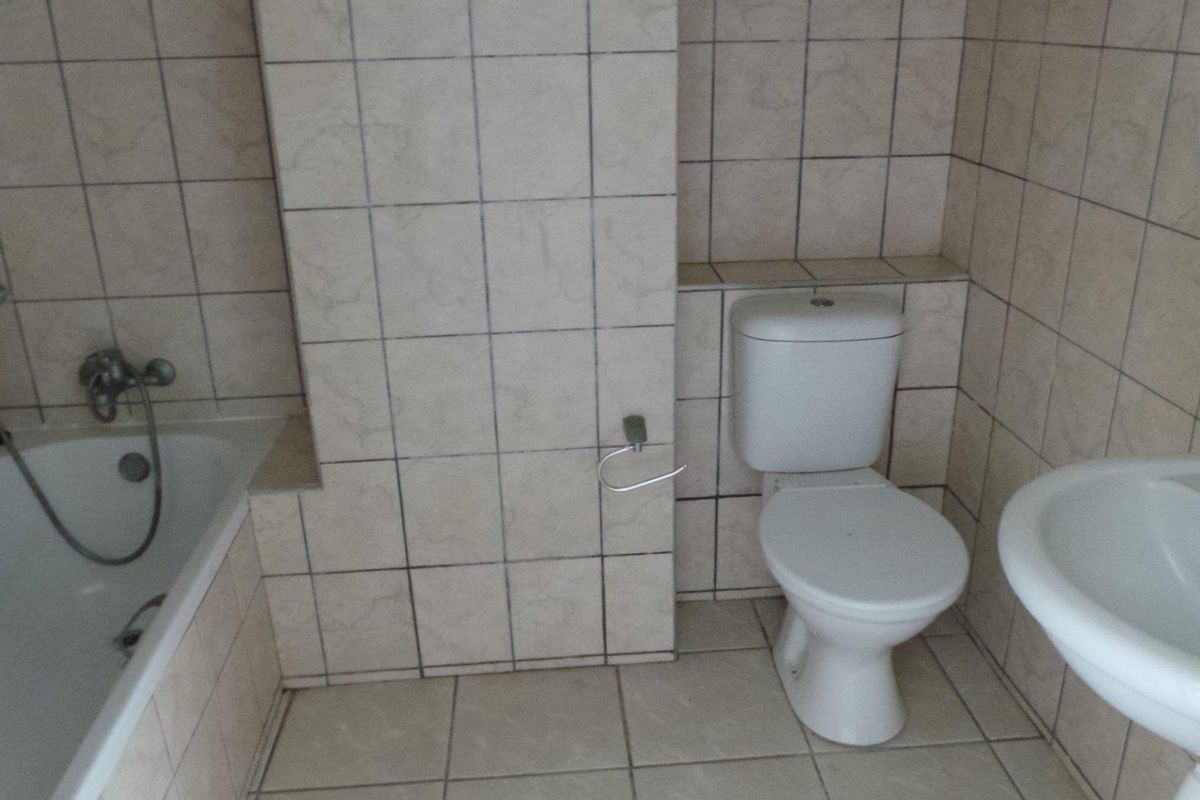 A functional bathroom featuring a standard bathtub, pedestal sink, and toilet, finished with neutral ceramic wall and floor tiles.