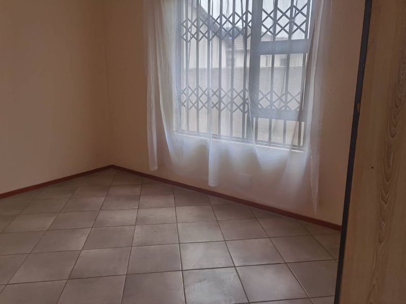 An empty bedroom featuring neutral tiled flooring and a window fitted with a security gate, offering a blank canvas for potential interior design.
