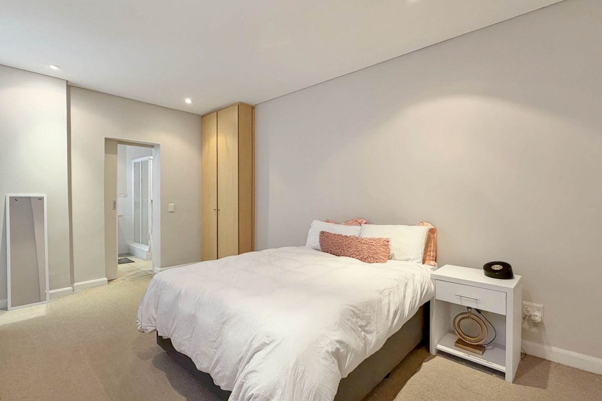 A well-maintained bedroom featuring neutral tones, carpet flooring, recessed lighting, and a built-in wardrobe with convenient access to an en-suite bathroom.