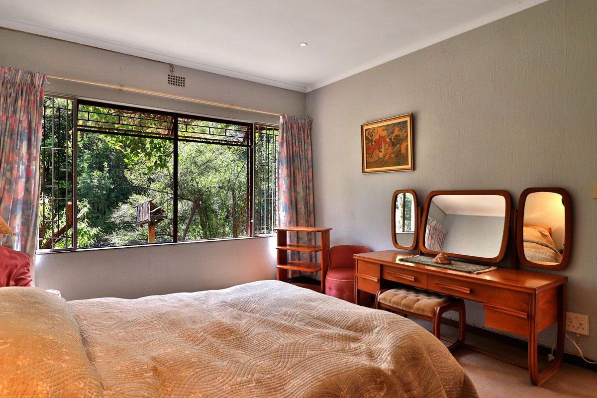 A well-lit bedroom featuring large windows with garden views, neutral wall tones, and carpeted flooring.
