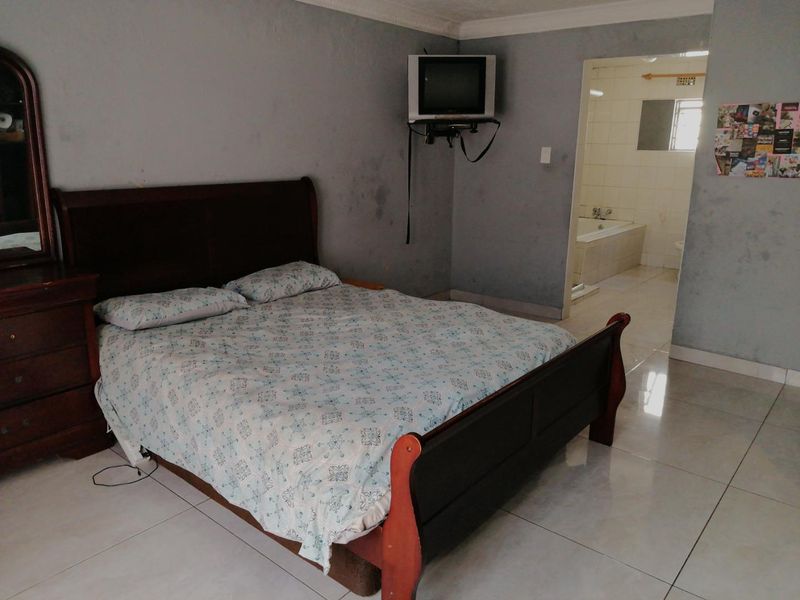 A bedroom featuring tiled flooring, crown molding, and an attached en-suite bathroom, showing signs of wear on the wall surfaces.