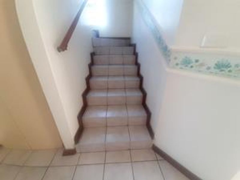 A tiled staircase featuring a wooden handrail and decorative wall border, providing access between levels in this townhouse.