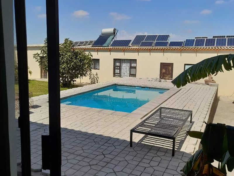 Outdoor pool area featuring a paved deck, solar panels, and solar water heating system, viewed from an interior sliding door.
