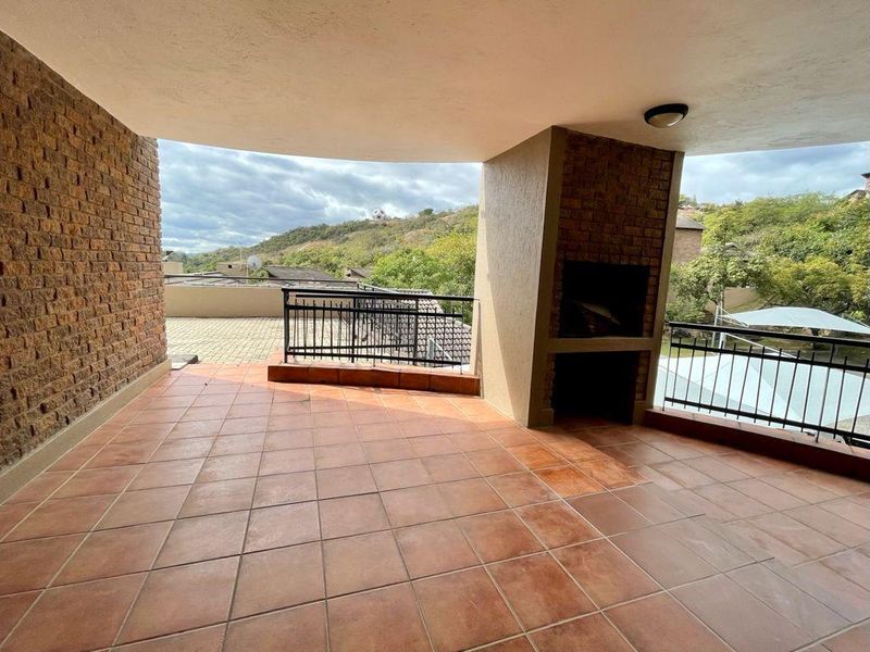 Spacious covered balcony featuring a built-in braai, terracotta tiled flooring, and a brick feature wall, offering an ideal space for outdoor entertaining.