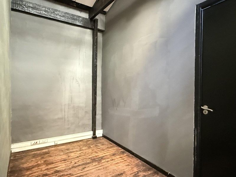 An empty office space featuring exposed timber beams, dark painted walls, and timber flooring, providing a blank canvas for professional use.