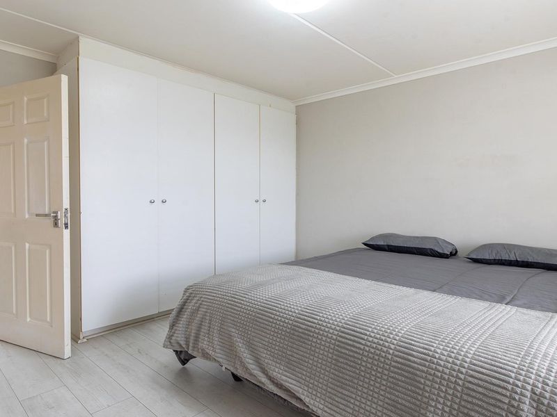 A bedroom featuring built-in cupboards and light-toned laminate flooring, with an adjacent view into a tiled bathroom area.