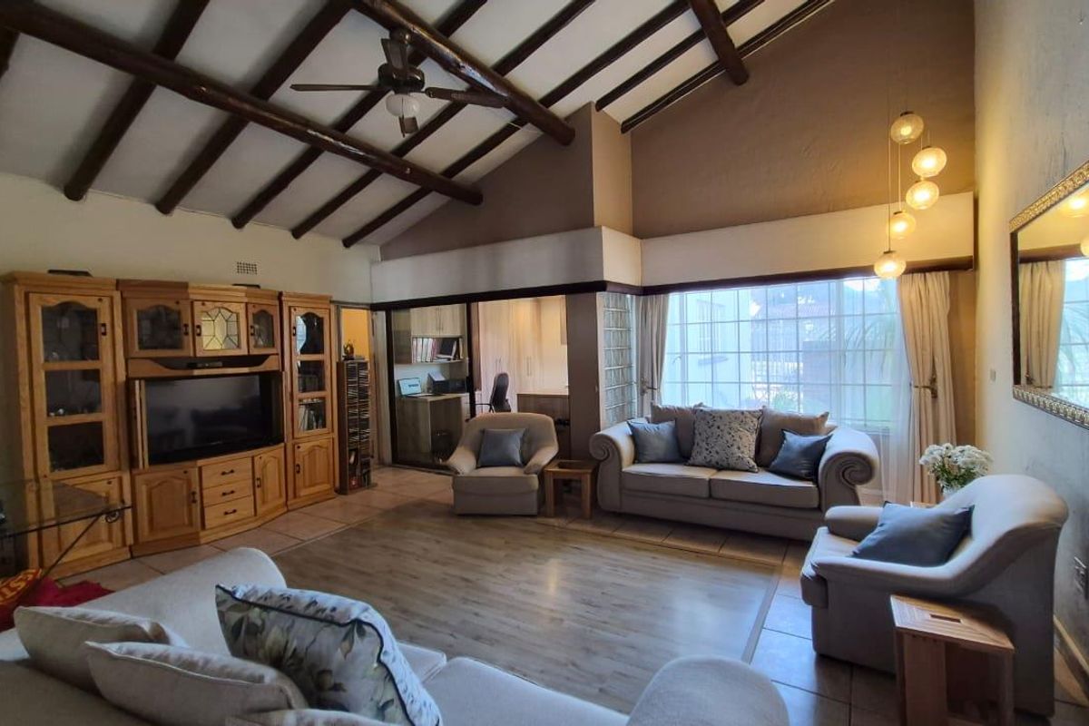 Spacious living room featuring high vaulted ceilings with exposed timber beams, a ceiling fan, and a unique glass block wall partition.